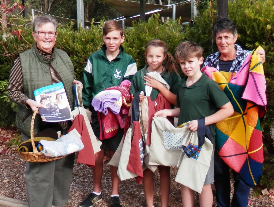 VIEW club members Susan Stephenson (left) and Rose Barker (right) hand over knitted and crocheted mats and rugs, and fabric library bags to Wyndham Public School students Tyler Thomas, Tamika Westaway and Zach Cox.