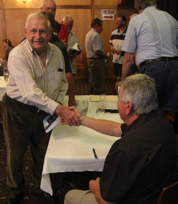 Lloyd Cocks congratulates Vic Jurskis. Background from left: Maree O’Neill busy selling books; Neil Rankin obscured, retired Bermagui forester Allan Douch and  retired harbour master Max Saunders line up for autographs;  Ross Dobbyns retired Regional Forester chatting with Forest Ecologist Pete Kambouris; mycologist Bob Weston with back to camera. Photo by Toni Ward.