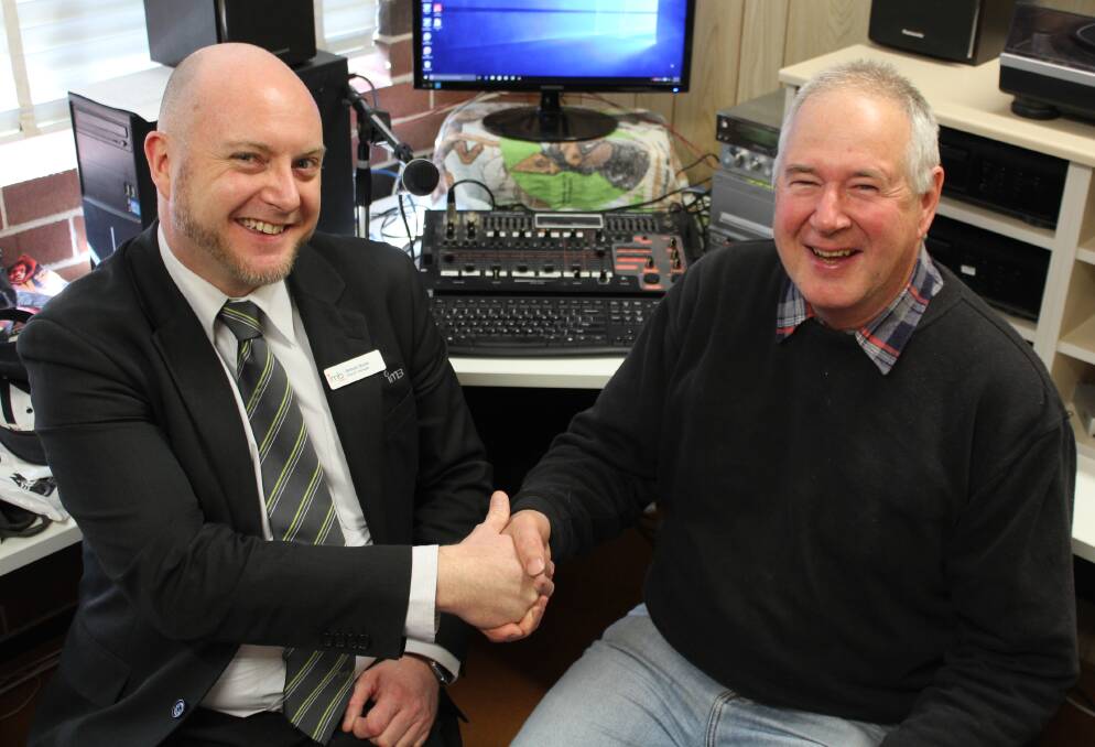 Hand shake: Eden IMB Bank branch manager Simon Dunn (left) with 2SEA Community Radio station manager Terry Love, seated in front of the old desk that is soon to be replaced, Monday August 29. Picture: Toni Houston