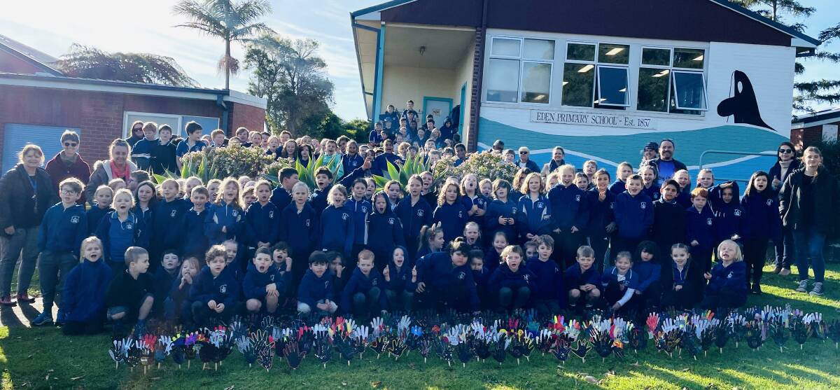 Eden Public School students and staff stand before the school in front of their Sea of Hands artworks painted by the students. Photo supplied. 