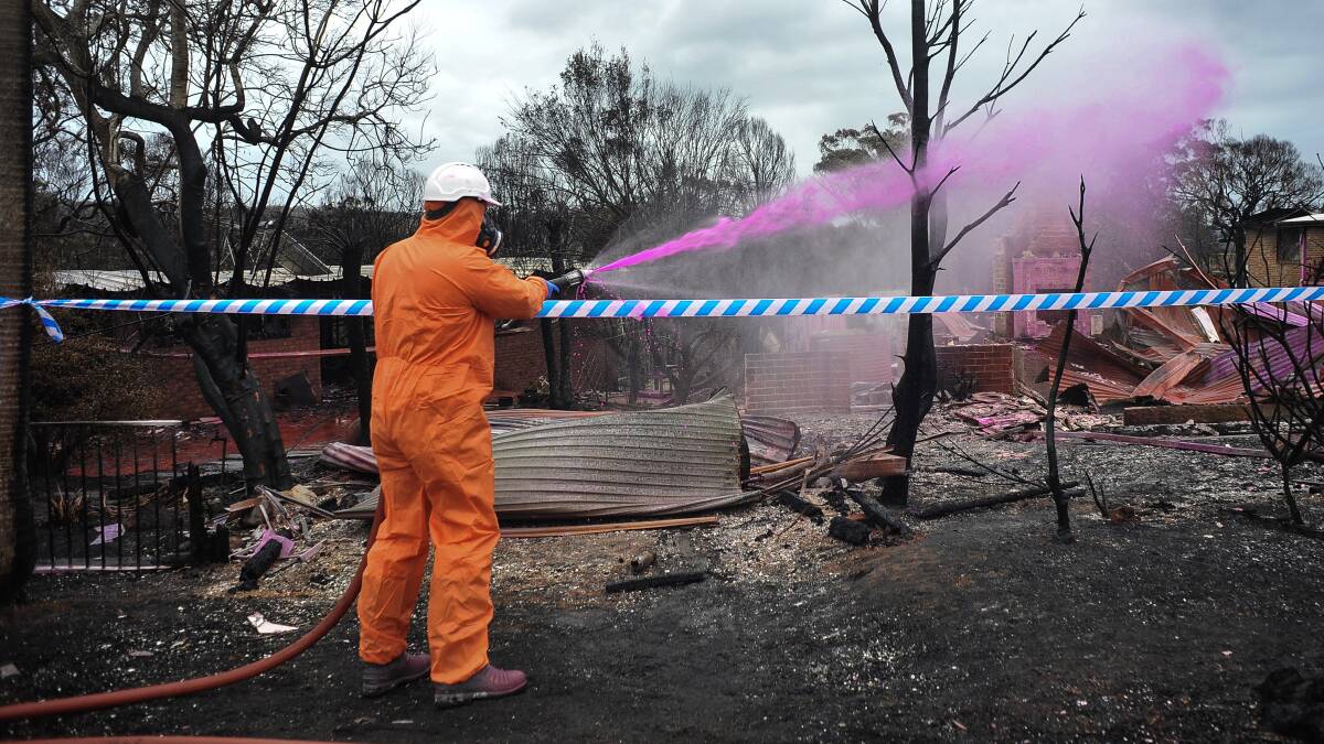 Clean-up workers spray an adhesive over asbestos-contaminated material in the wake of the bushfire at Tathra. Picture: AAP/Perry Duffin