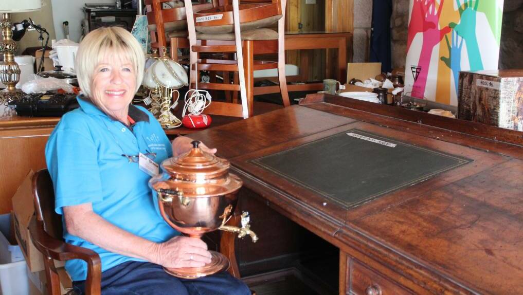 Ann Brosnan sits at an antique desk with a 19th century samovar, two unique items at the Samaritan Op Shop in Pambula..