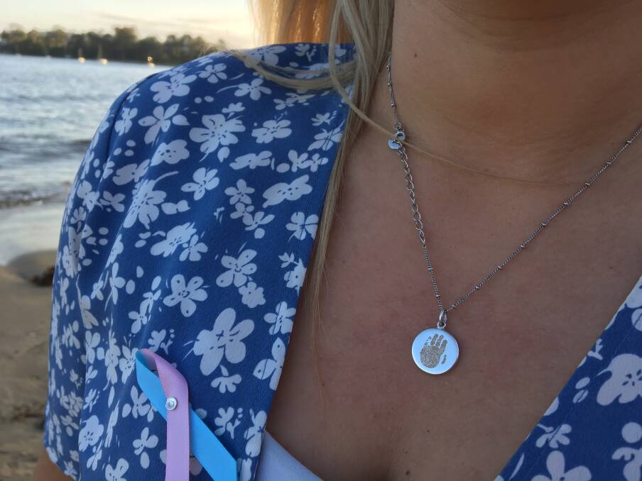 Jenna Lantouris wears a necklace of baby Kora's handprint and a pin for Pregnancy and Infant Loss Awareness month.