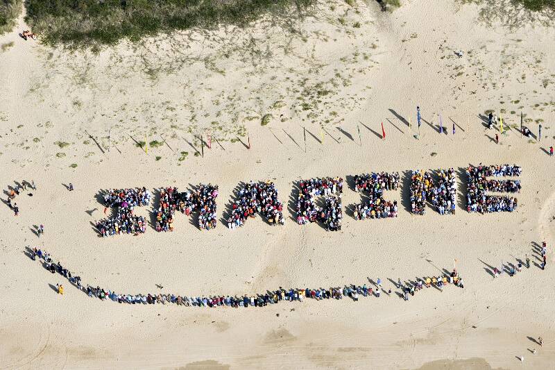 ON THE BEACH: More than 3000 people form one of two human signs on Tathra Beach in 2006, demonstrating the community’s commitment to renewable energy.